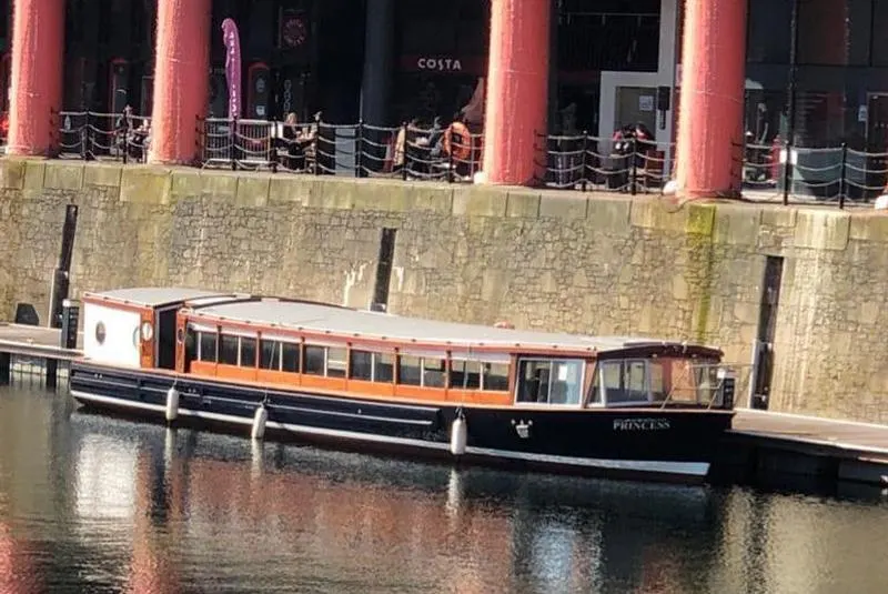 Passenger pleasure boat moored at a waterside promenade with red pillars and seating terraces above.