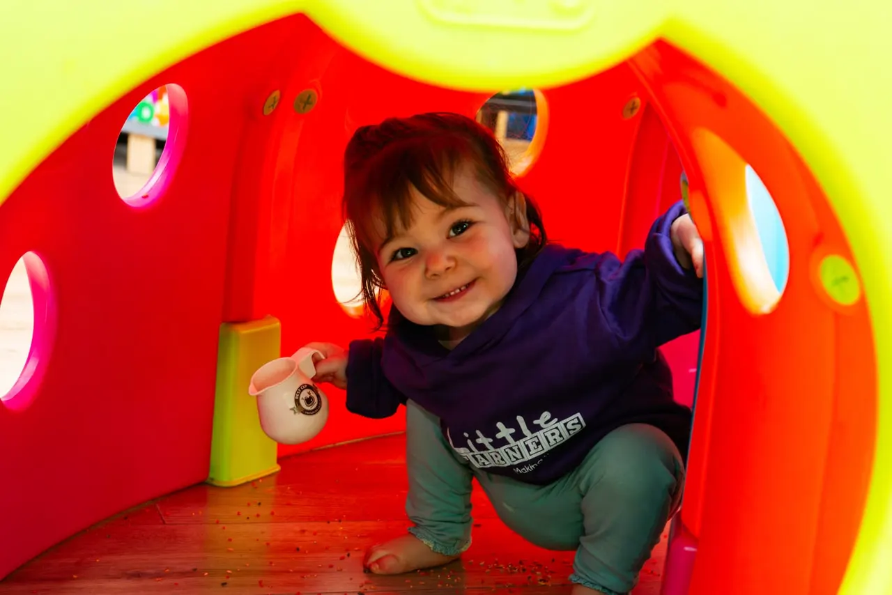 Toddler playing inside a brightly lit red tunnel with interactive sensory features and coloured lights.