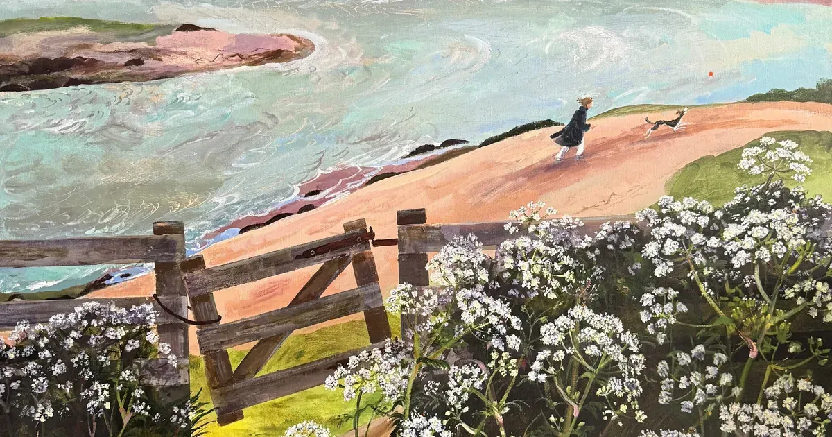 A figure and small dog walk on a sandy beach beside turquoise water, viewed past a wooden fence and white wildflowers.