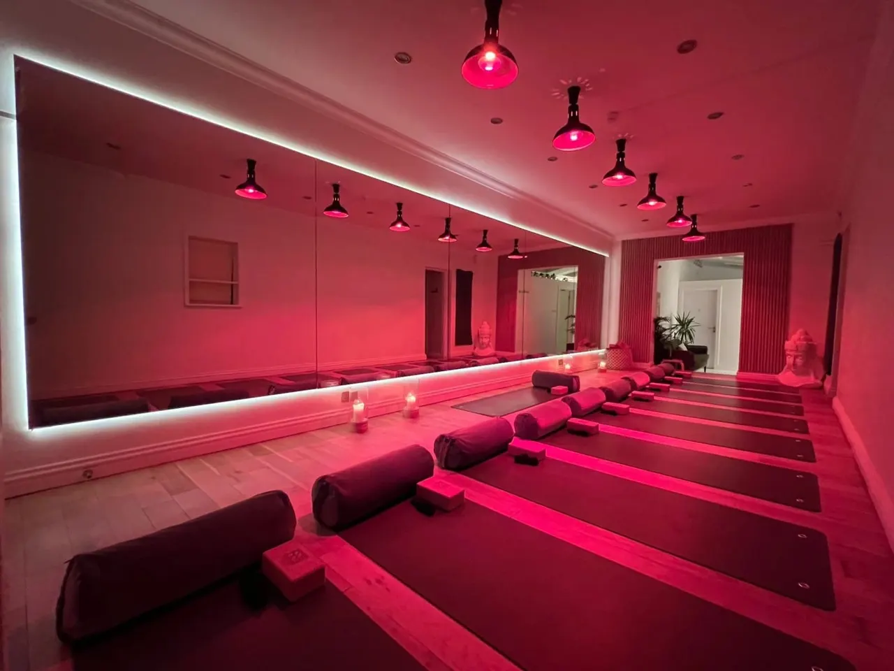 Modern yoga or fitness studio with rows of mats and bolsters lit by vibrant pink neon lighting and pendant lamps.