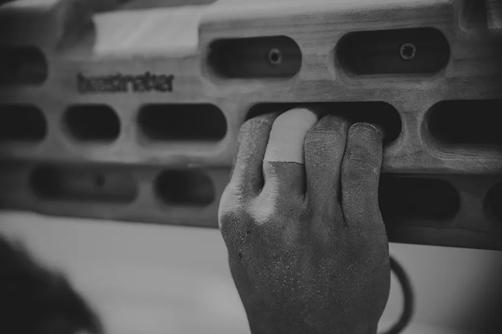 Close-up of a climber's dusty hand gripping a climbing wall hold.