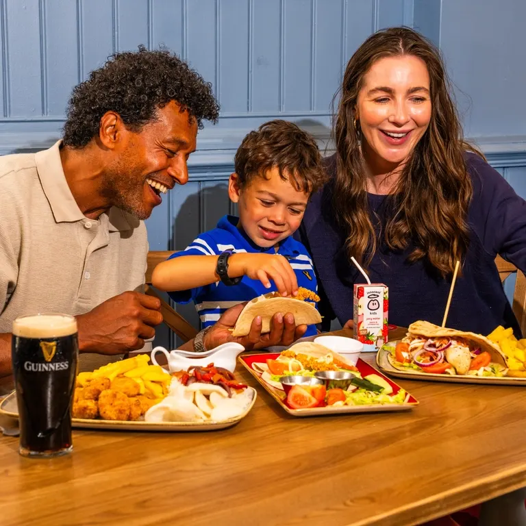 Family of three enjoying a meal together at a table with food and drinks.