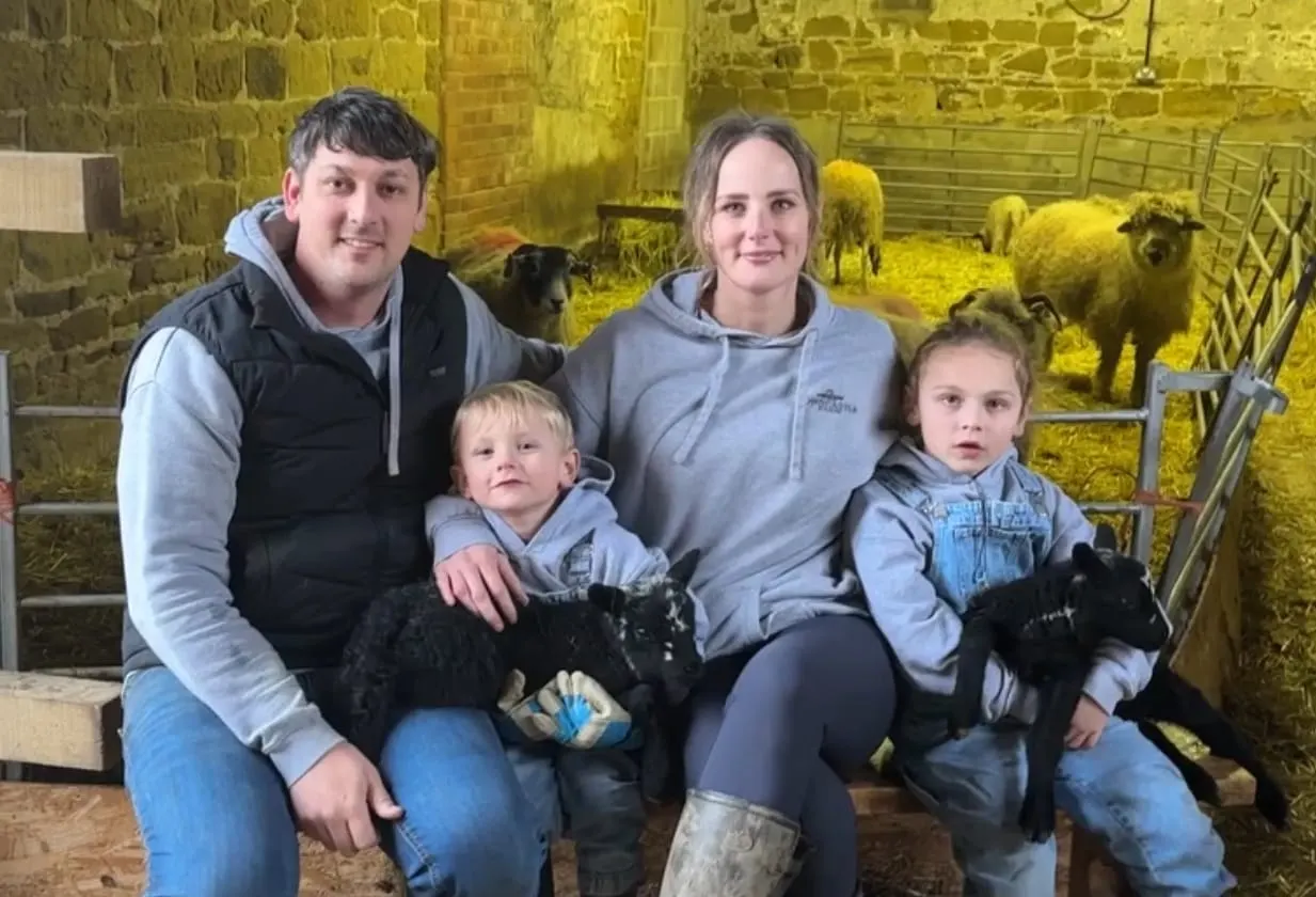 Family of four posing with young farm animals in a stone barn lit by yellow lighting.