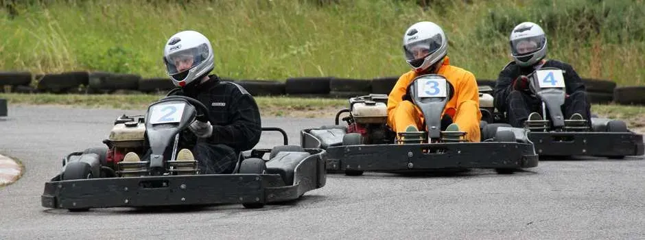Three people in helmets racing go-karts on an outdoor track.