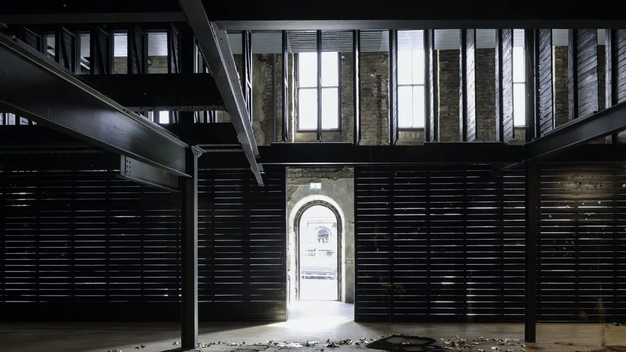 This is a PHOTOGRAPH.

Industrial interior space with black slatted walls and arched doorway leading to exterior light.