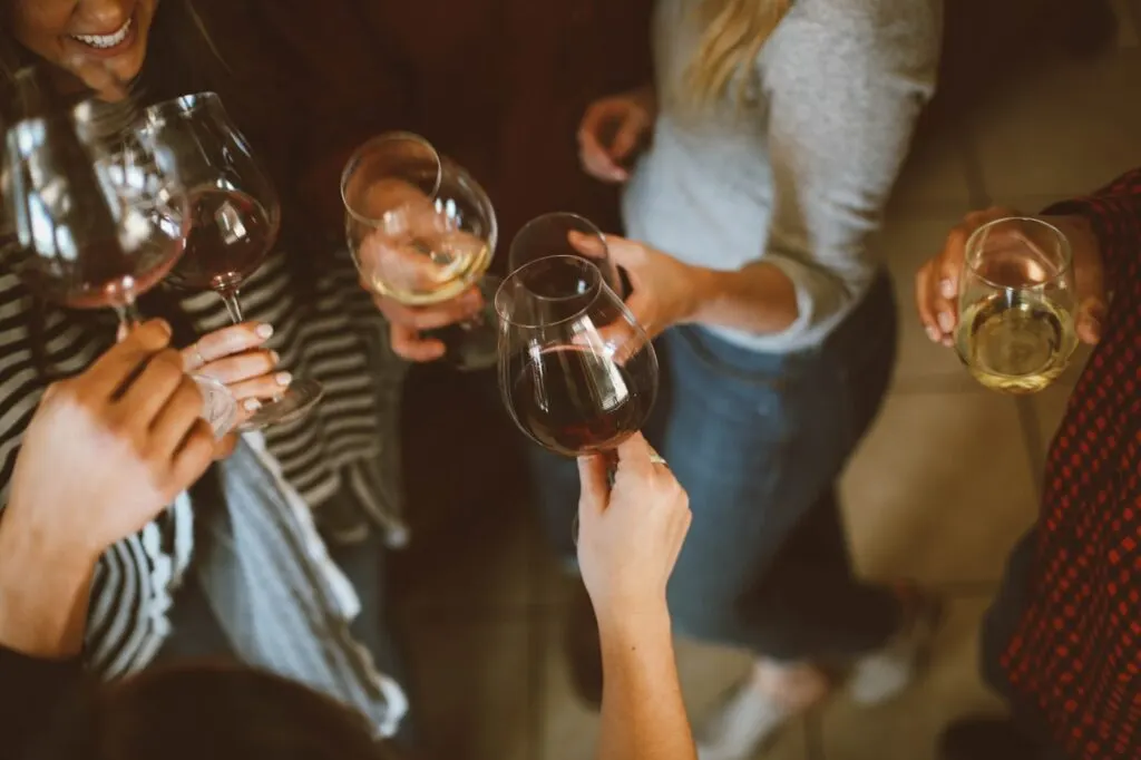 Group of people holding wine glasses together in a toast at an indoor social gathering.