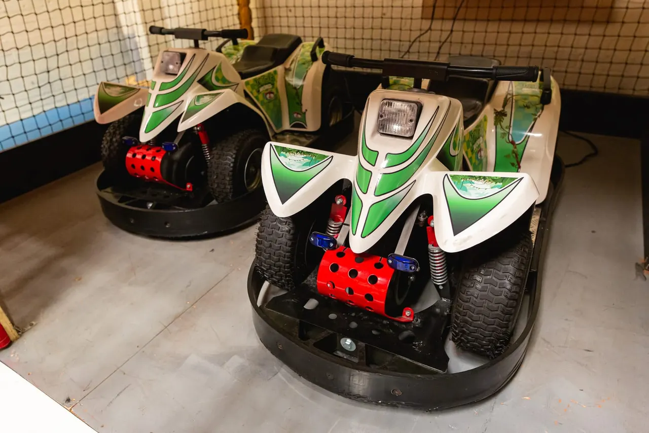 Electric bumper cars with green and white bodywork parked in an indoor arena with safety netting.