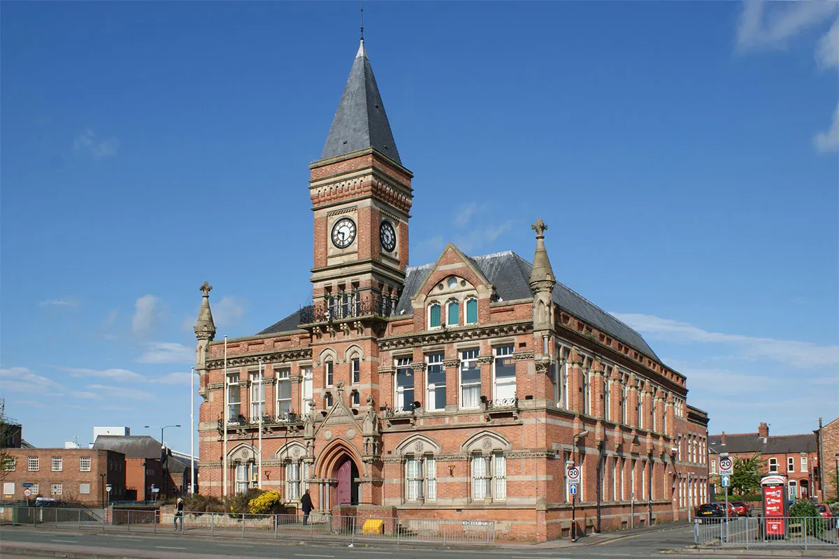A grand Victorian red-brick building with a prominent clock tower, ornate architectural details and turrets under a clear blue sky.