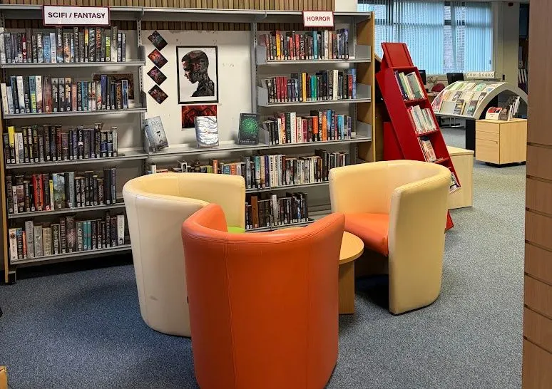 Library reading area with comfortable seating pods and shelves of books in the sci-fi/fantasy section.