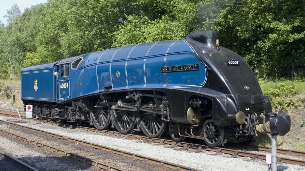 A blue and black streamlined steam locomotive numbered 60007 on display track with green trees in background.