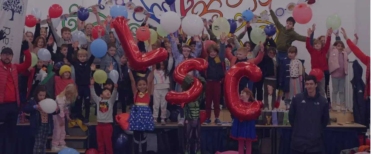 Large group of children celebrating with colourful balloons and giant red number balloons at an indoor event.