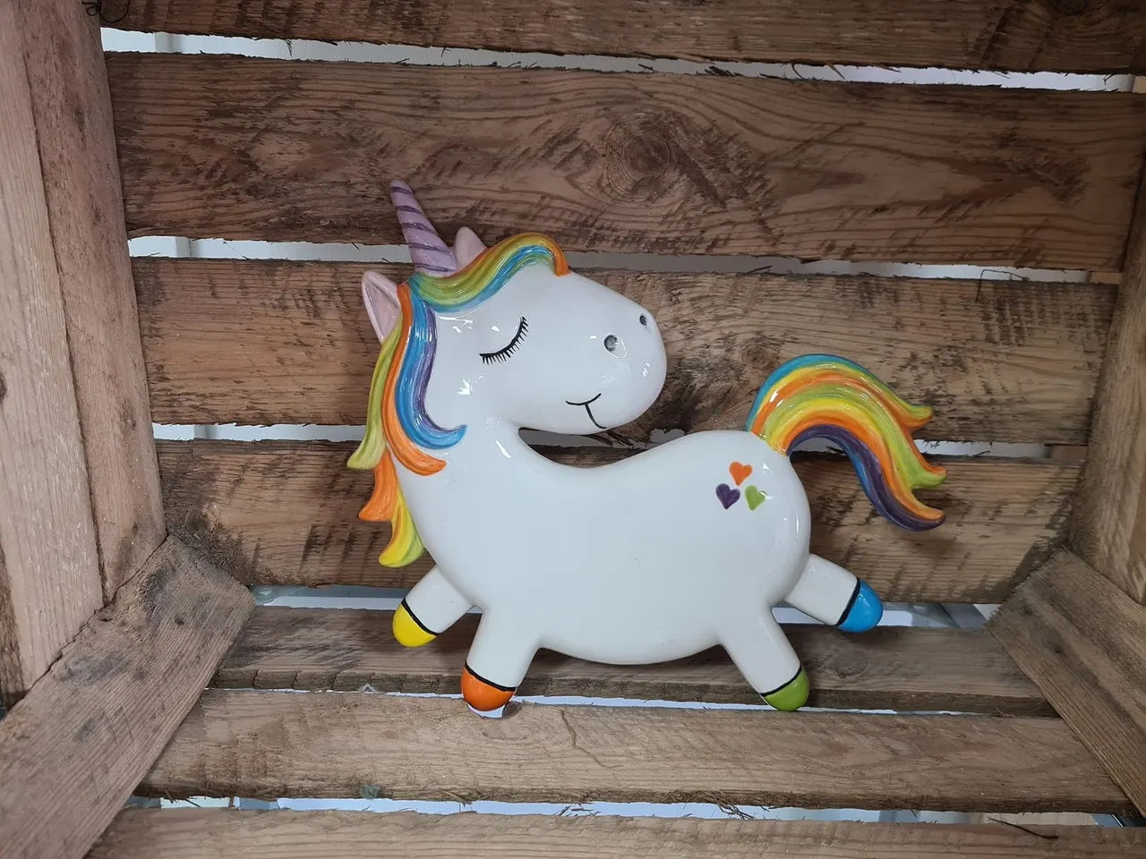 Decorative white unicorn figurine with rainbow mane and tail on wooden shelving.
