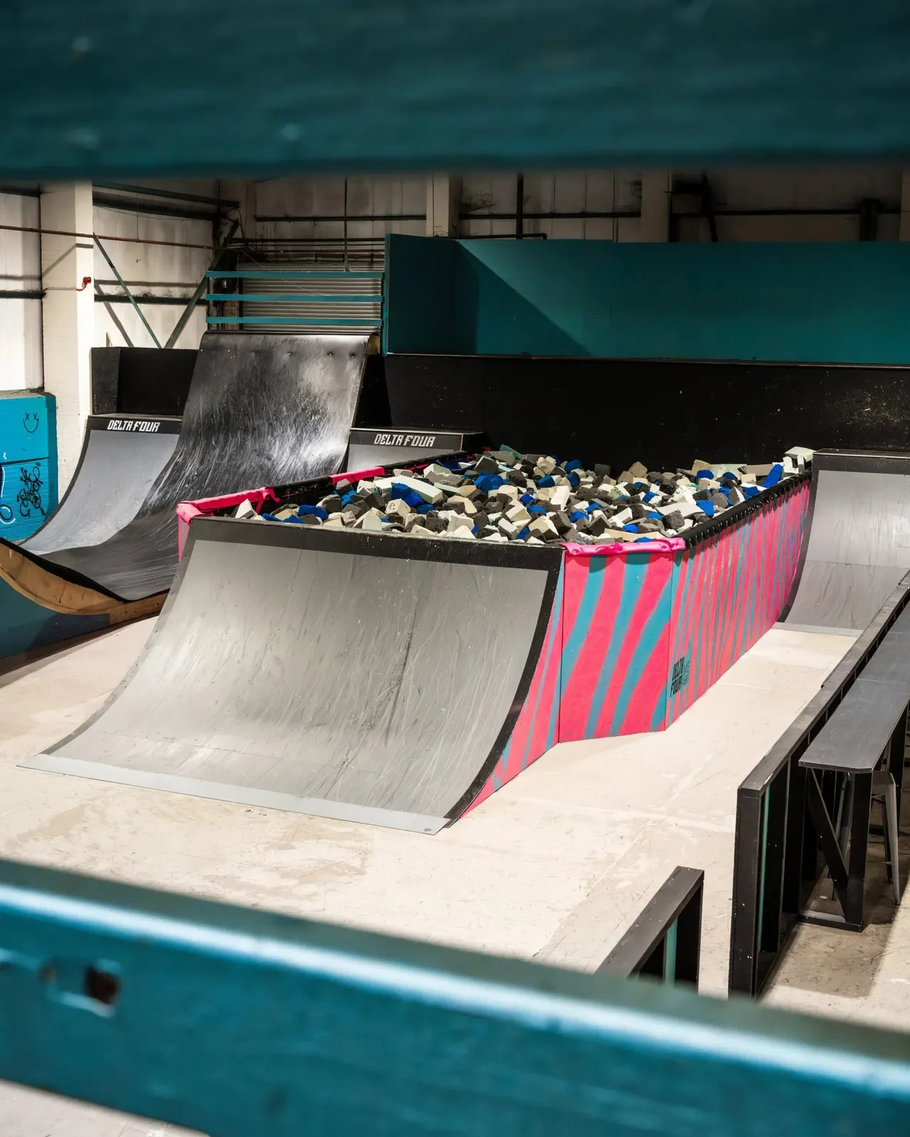 Indoor skate park with ramps and a foam pit filled with coloured blocks.