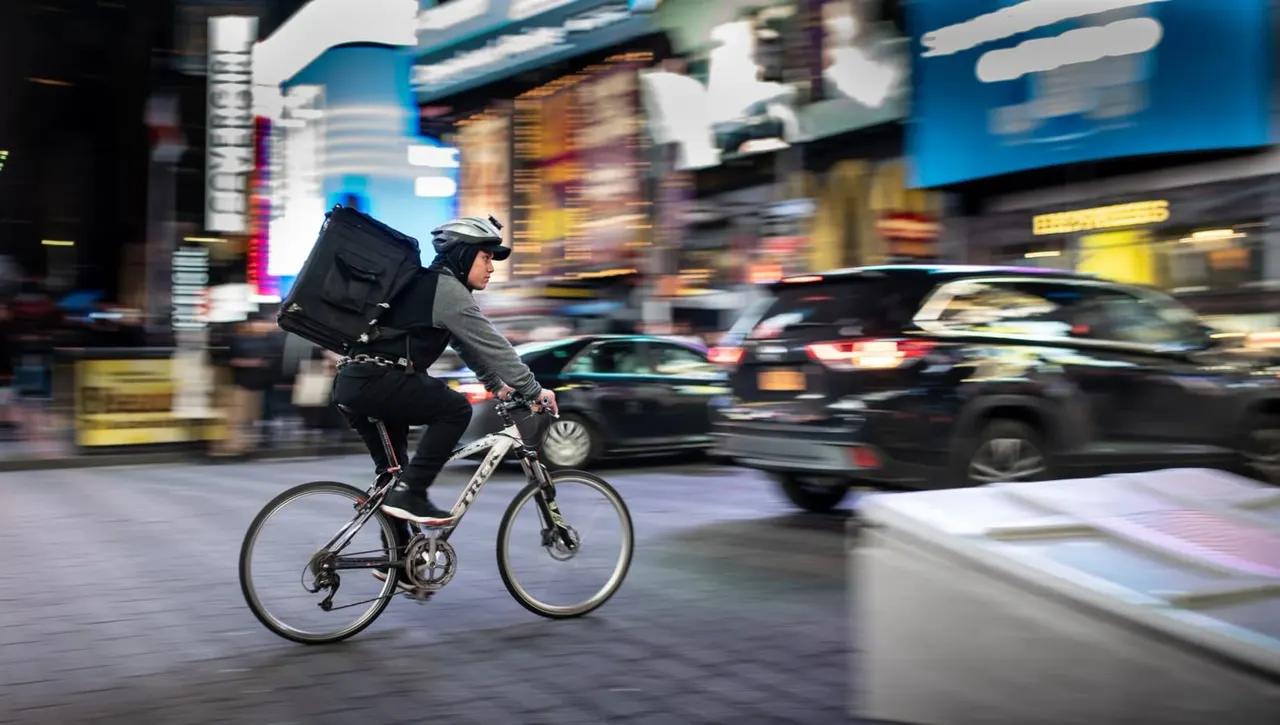 Person cycling through a busy urban street at night with traffic and illuminated buildings in the background.