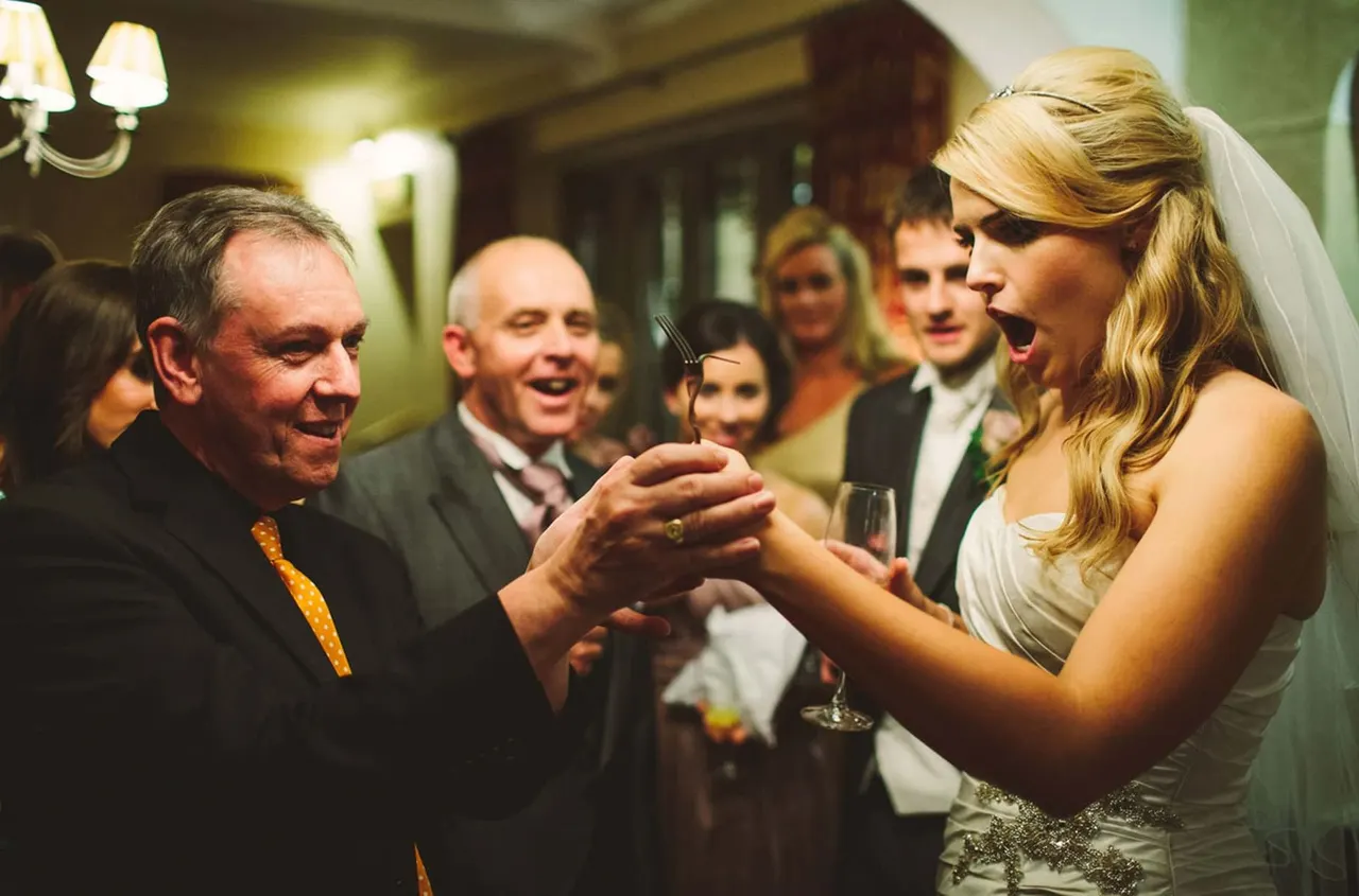 Bride in white dress and veil chats with guests holding a cocktail at an indoor wedding reception.