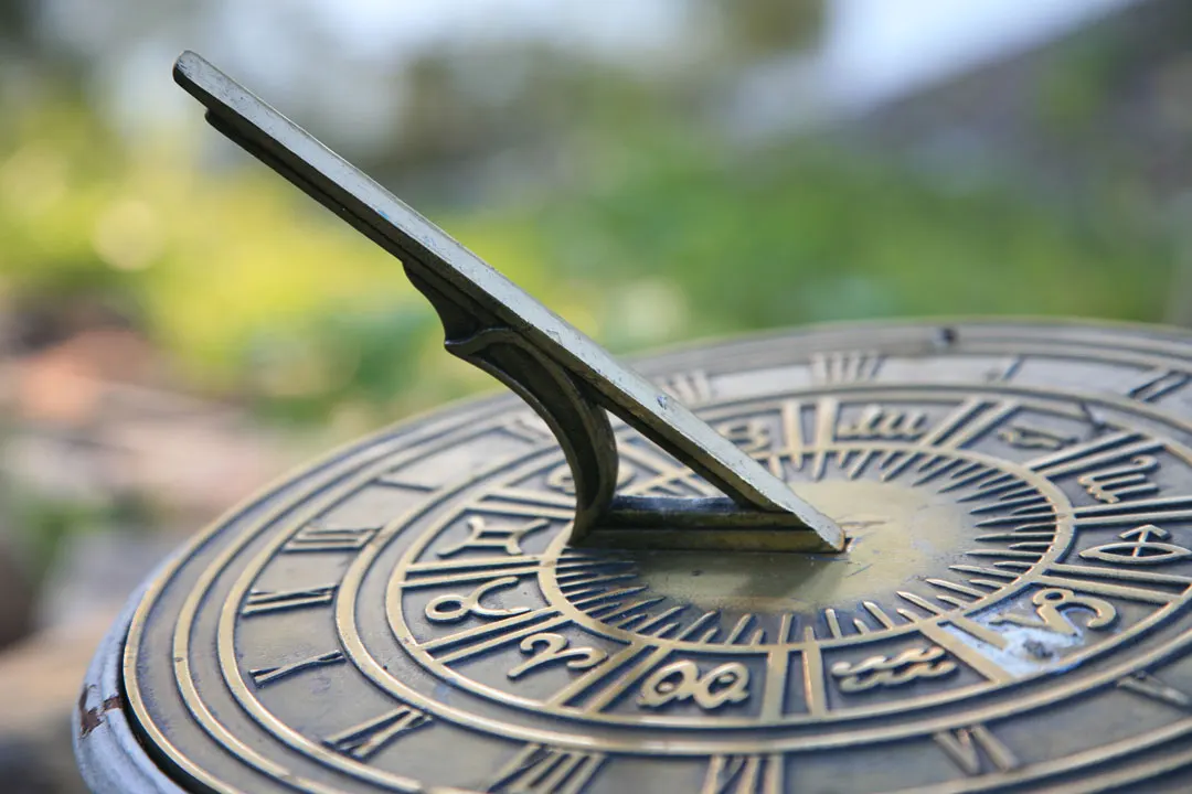 Close-up of a weathered brass sundial with engraved zodiac markers in a garden setting.