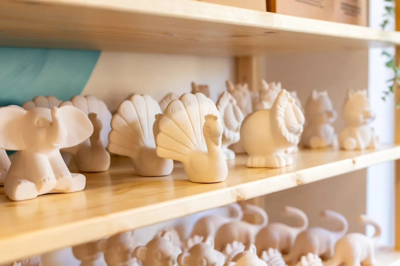 Wooden shelves displaying rows of unpainted ceramic bird figurines in cream and white tones.
