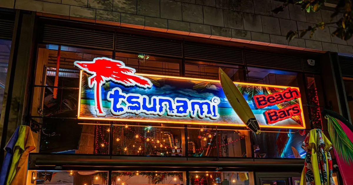 Neon signage for a beach bar venue displaying a red palm tree, blue text, and surfboard graphics at night.