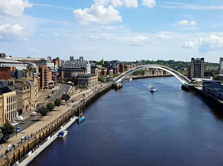 Aerial view of Newcastle's riverside with the Gateshead Millennium Bridge spanning the river and historic quayside buildings.