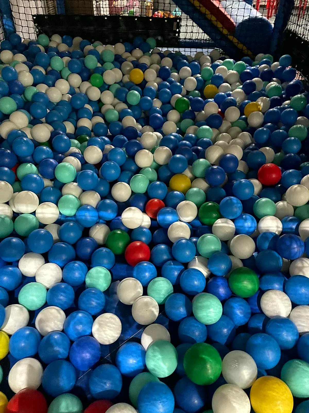 Ball pit filled with blue, white, green, yellow and red plastic balls enclosed by netting.
