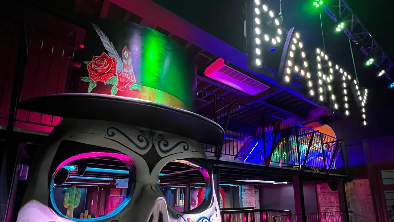 Nighttime exterior of entertainment venue illuminated with vibrant neon lighting in pink, green, purple and blue.