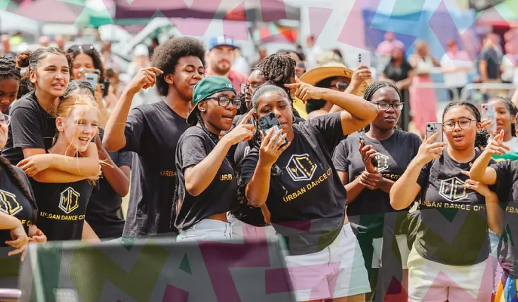 Group of young people wearing matching black "Urban Dance City" t-shirts dancing and celebrating together at an outdoor event.