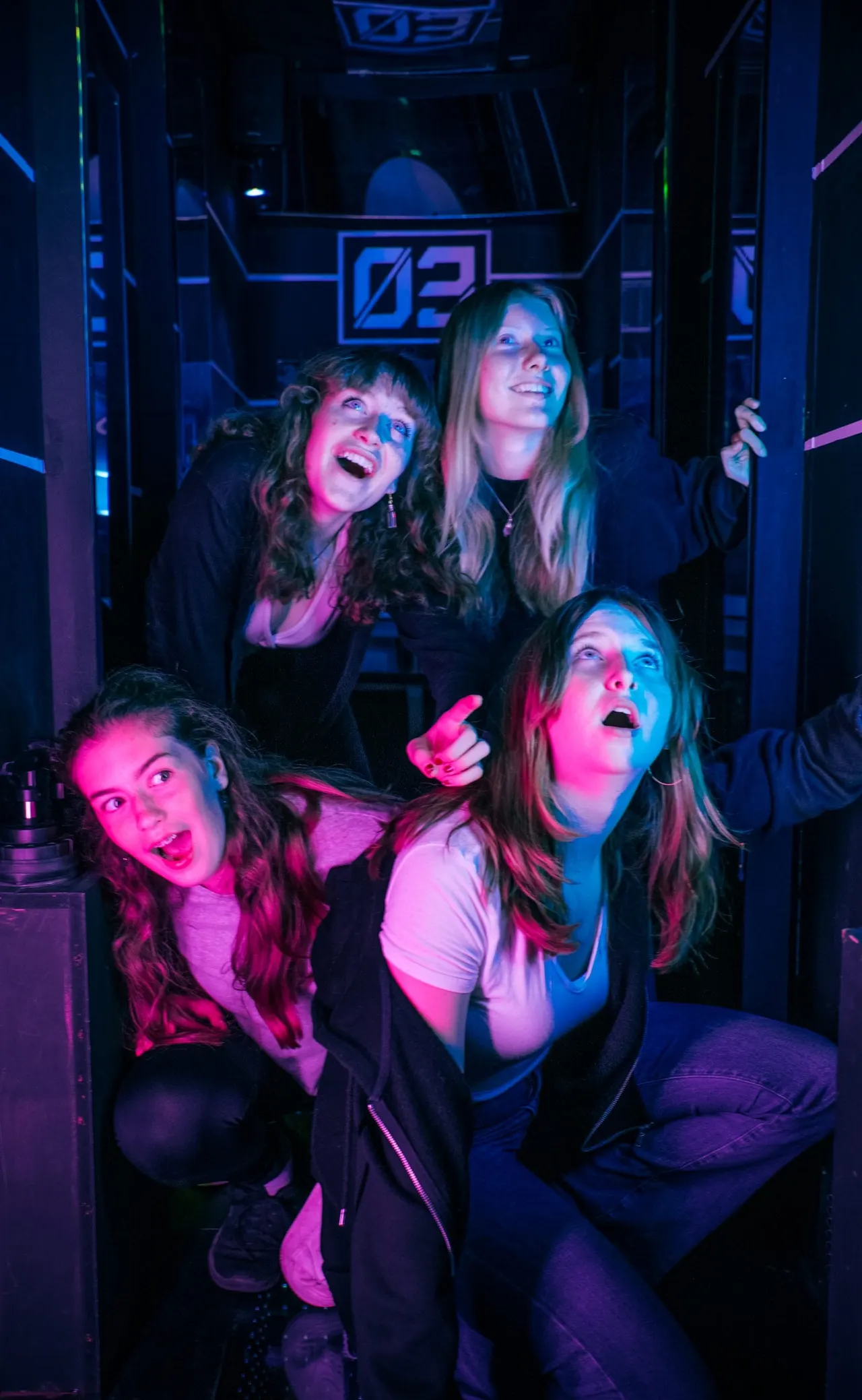 Four people playing laser tag in a neon-lit arcade game pod with blue and pink lighting.