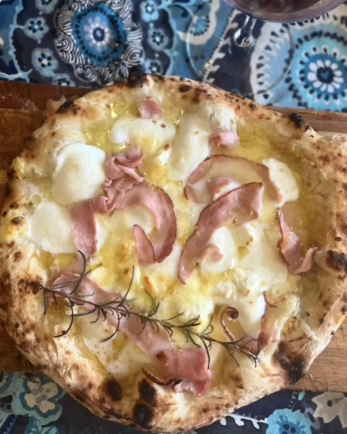 Freshly baked pizza topped with cheese, cured meat and rosemary on a wooden board.