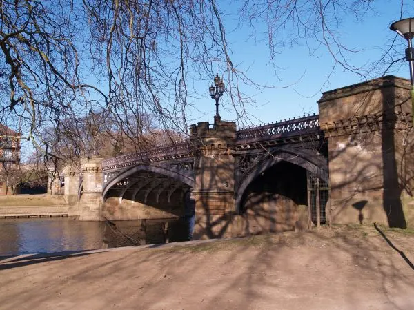 Stone bridge spanning a river with bare winter trees overhead and sandy ground in foreground.