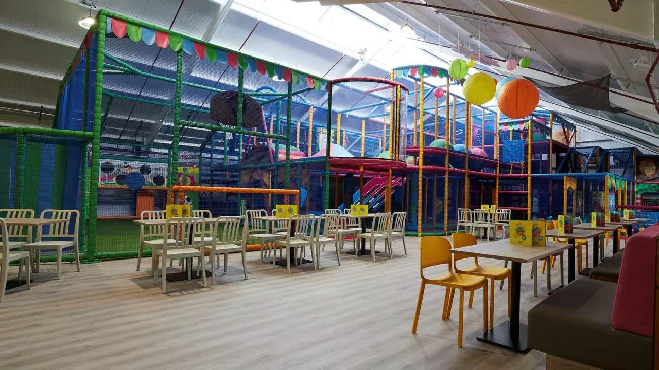 Indoor soft play facility with multi-level climbing structures, seating areas, colourful lantern decorations and tables for families.