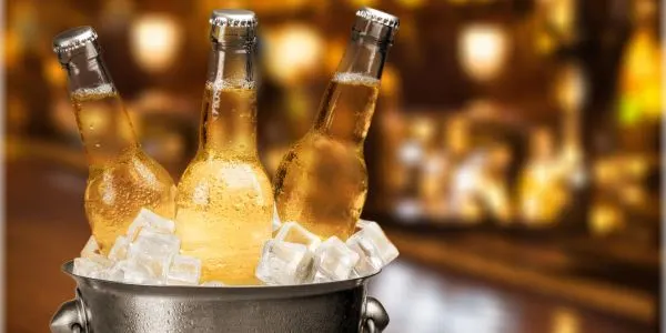 Three chilled beer bottles in an ice bucket in a warmly lit bar setting.