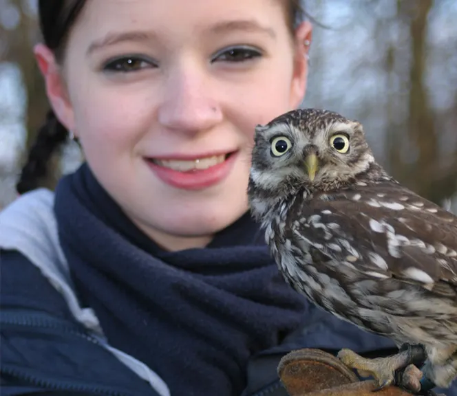Young person smiling whilst holding a small owl on their gloved hand outdoors.