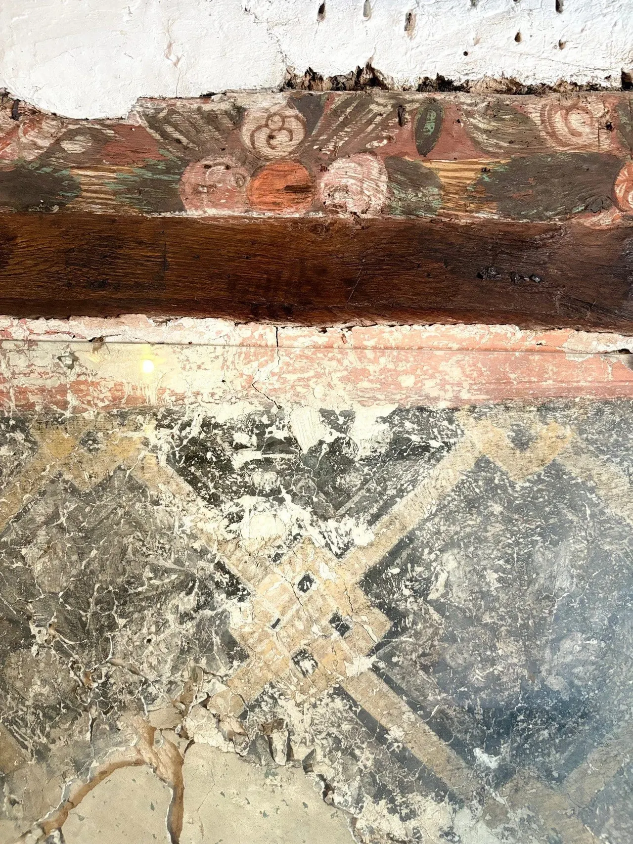 Close-up of weathered wooden beams and painted plasterwork showing layers of aged paint and decorative markings on a historic building interior.