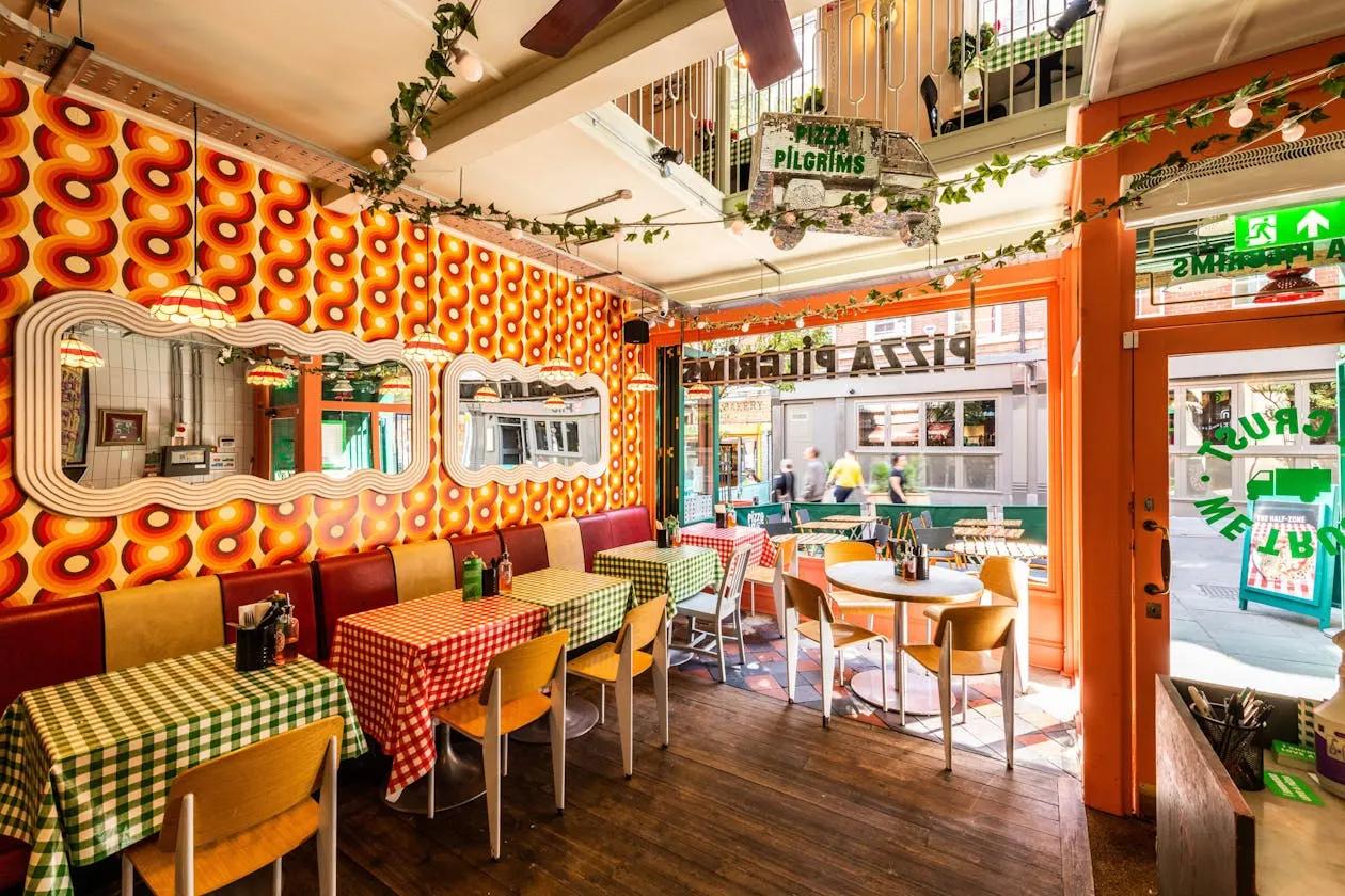 Colourful retro-style restaurant interior with orange patterned wall, checkered tablecloths and wooden chairs at dining tables.