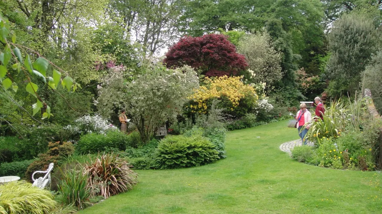 Two visitors walk through a landscaped garden with flowering shrubs, specimen trees and manicured lawn.