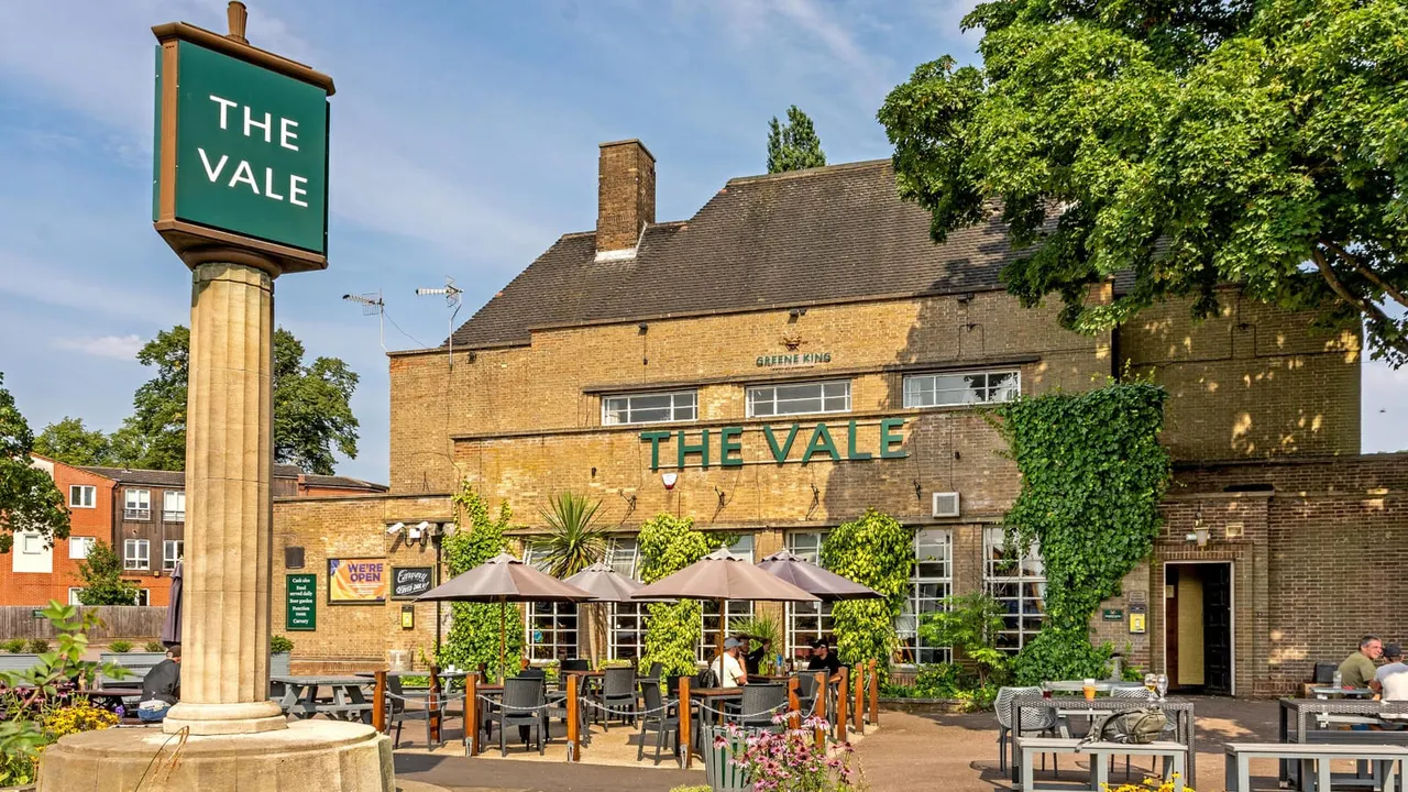 Pub's outdoor terrace with customers seated under umbrellas, ivy-covered brick building, and green signage on sunny day.