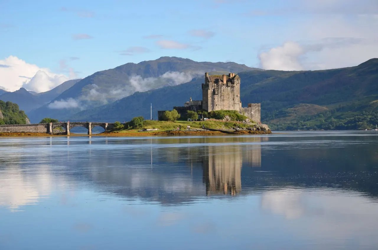 Medieval castle on an island in a Scottish loch, with mountains in the background and calm water reflecting the stone structure.