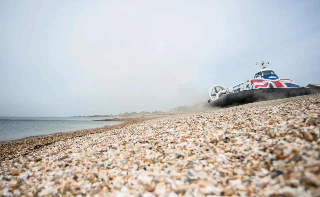 Hovercraft with Union Jack livery beached on shingle beside calm sea.
