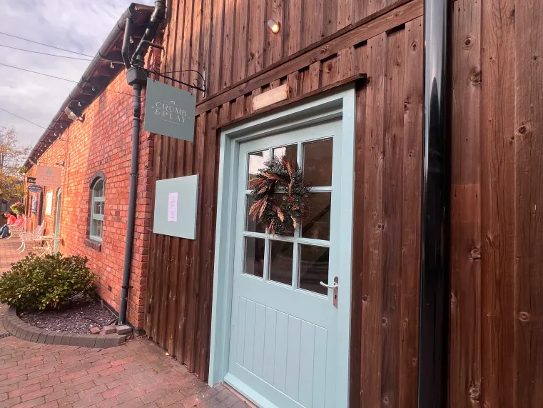 Exterior of a leisure venue with a light blue door and wreath, featuring brick and wooden cladding architecture.