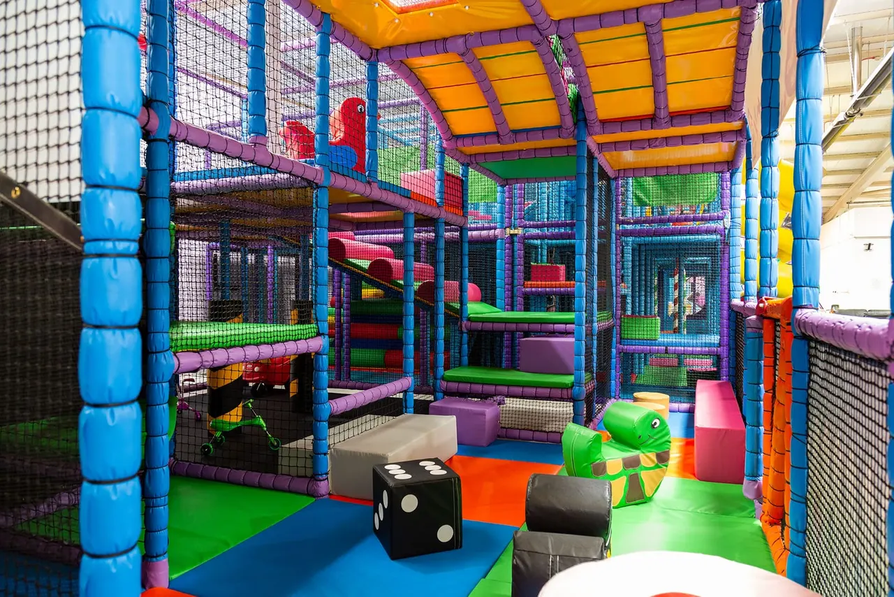 Colourful soft play structure with climbing frames, netting, slides and foam blocks in brightly coloured purple, blue, orange and green.