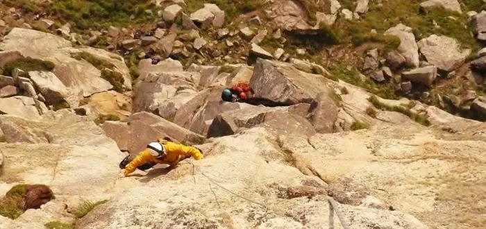 Rock climbers ascending a rocky cliff face using ropes and safety equipment.