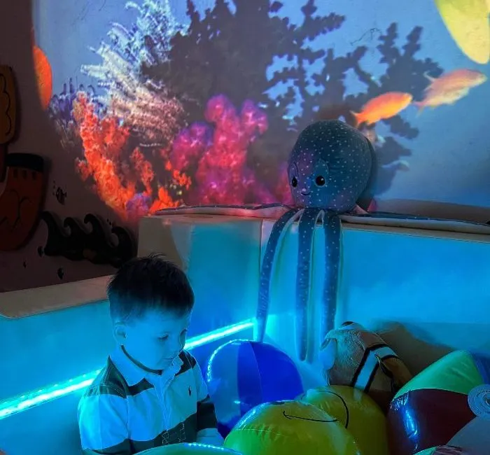 Young child exploring illuminated interactive display with glowing octopus figure and projected underwater scene.