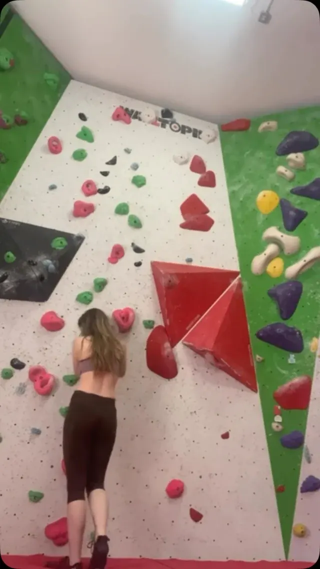 Child climbing an indoor rock wall with colourful handholds under artificial lighting.