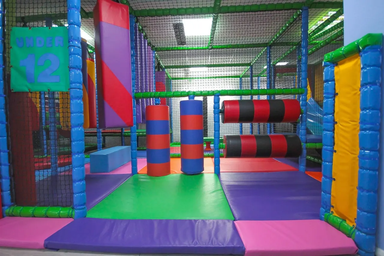 Interior of a colourful soft play facility with foam obstacles, tunnels and climbing structures for children.