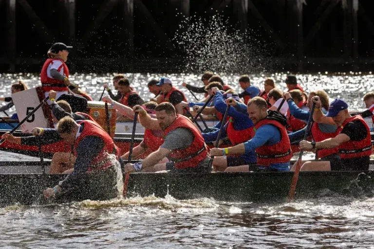 Dragon boat racers paddle through water while splashing during a competitive race.