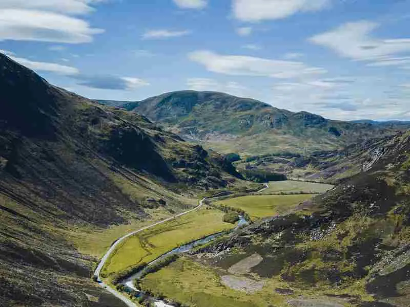 Valley landscape with winding river, green fields, and hills under blue sky.