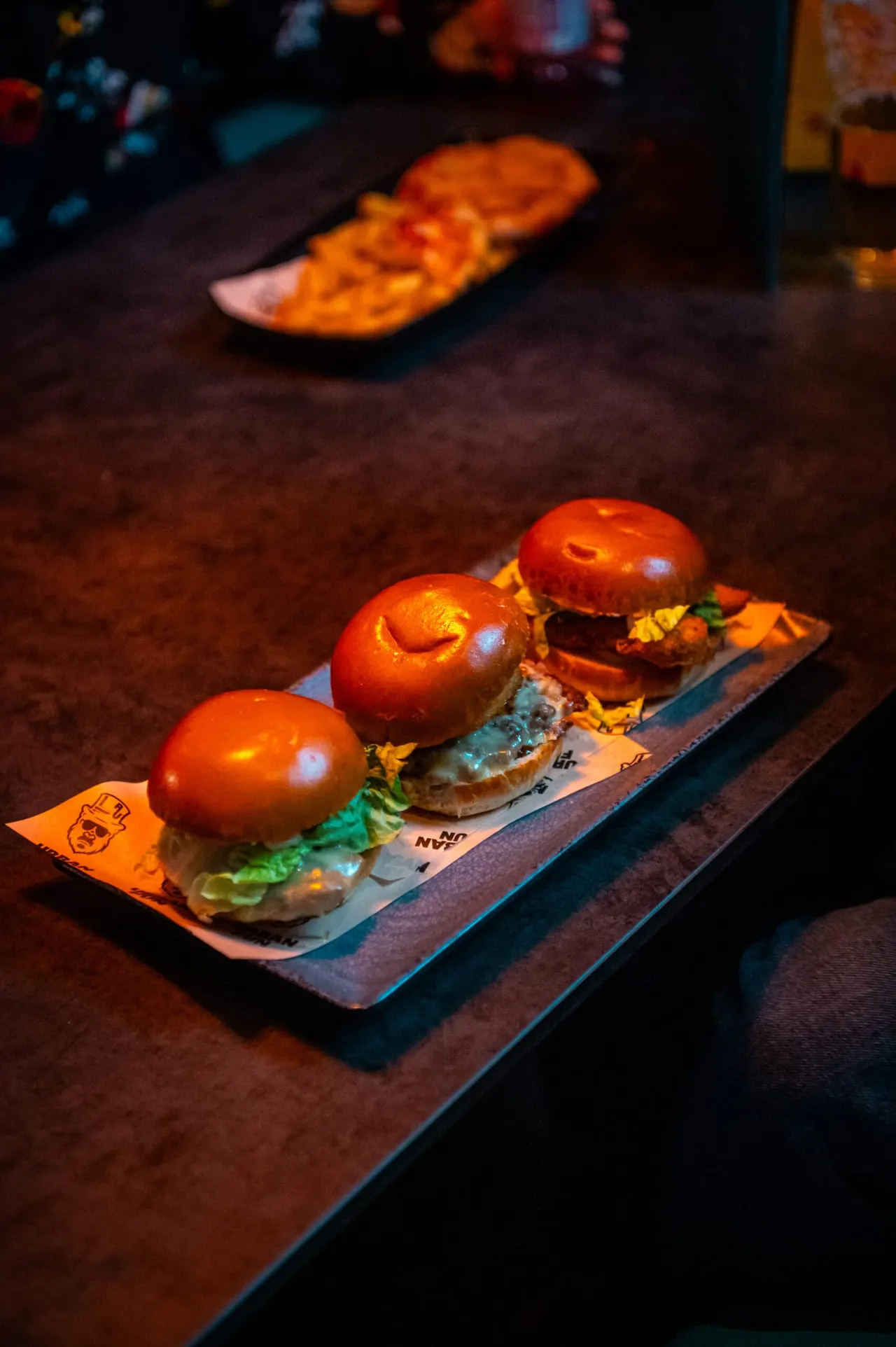 Three burgers with glowing red buns served on a wooden board in dim lighting.