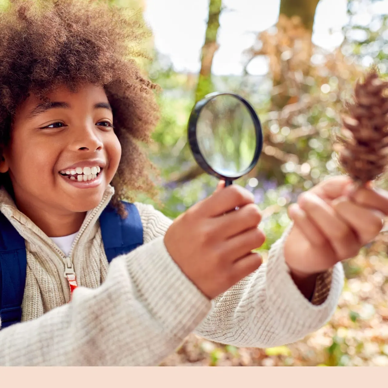 Child holding a magnifying glass while exploring plants and trees outdoors in a garden setting.