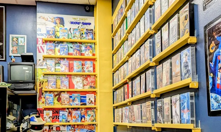 Retro gaming arcade interior with yellow shelving displaying vintage video game boxes and a CRT monitor on the left.