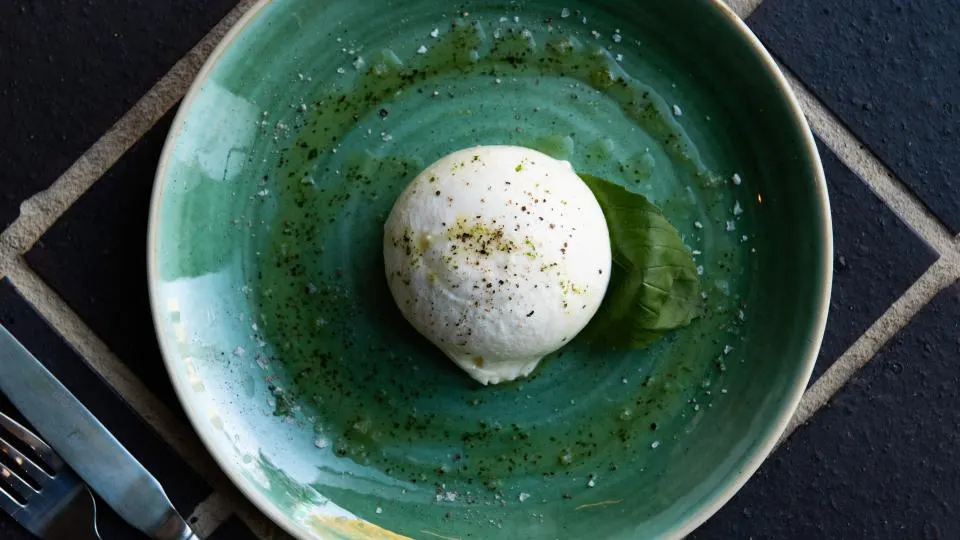 Burrata cheese with herbs on a green ceramic plate served as a dish.